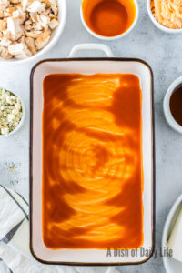 Buffalo sauce spread over the bottom of a casserole dish.