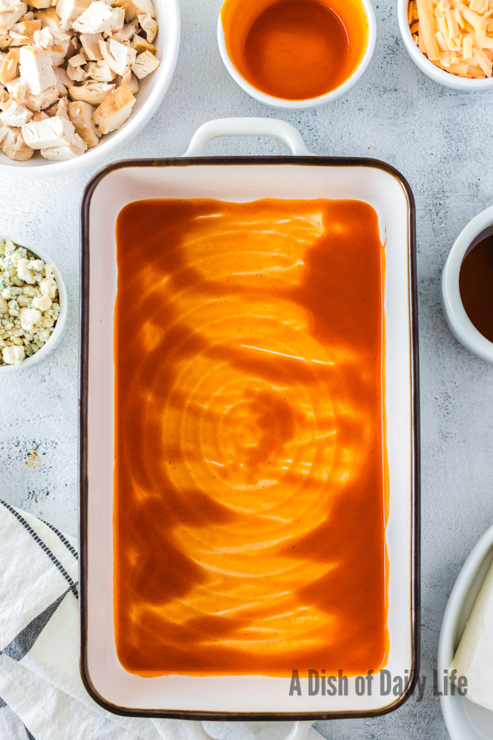 Buffalo sauce spread over the bottom of a casserole dish.