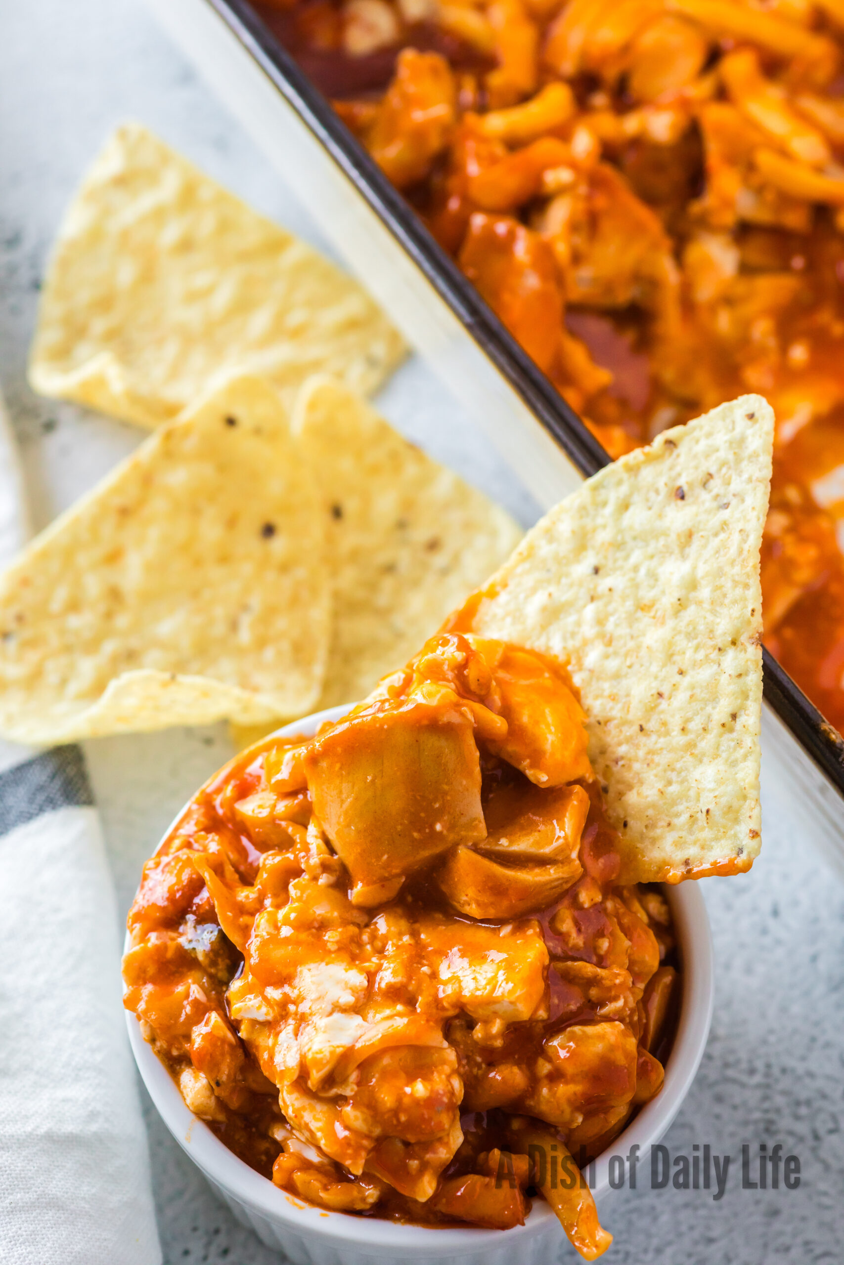 A bowl full of chicken dip with a tortilla chip sticking out of it.