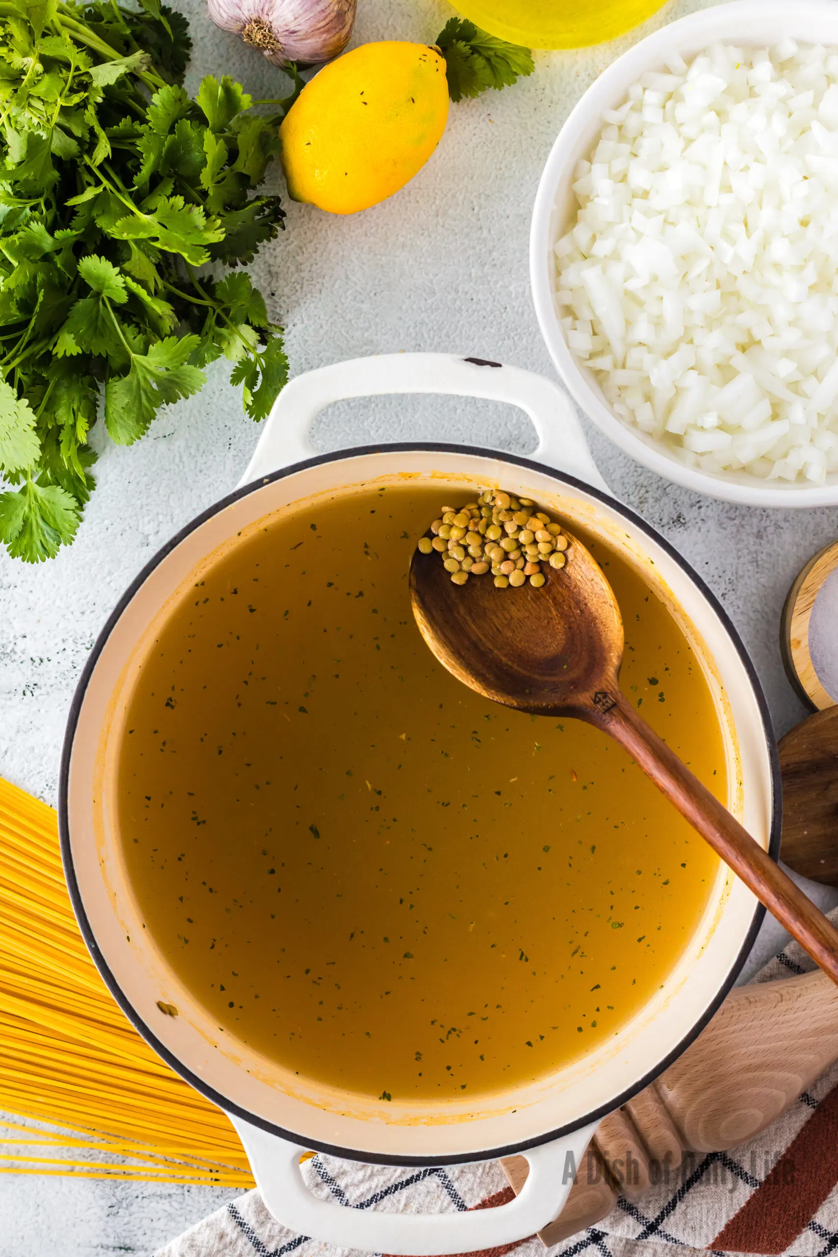 spoon placing rinsed lentils in pot of broth