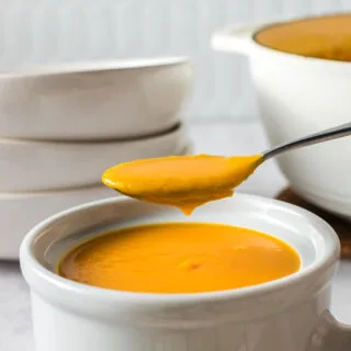 side view of a bowl of soup with a spoon full held above the bowl.