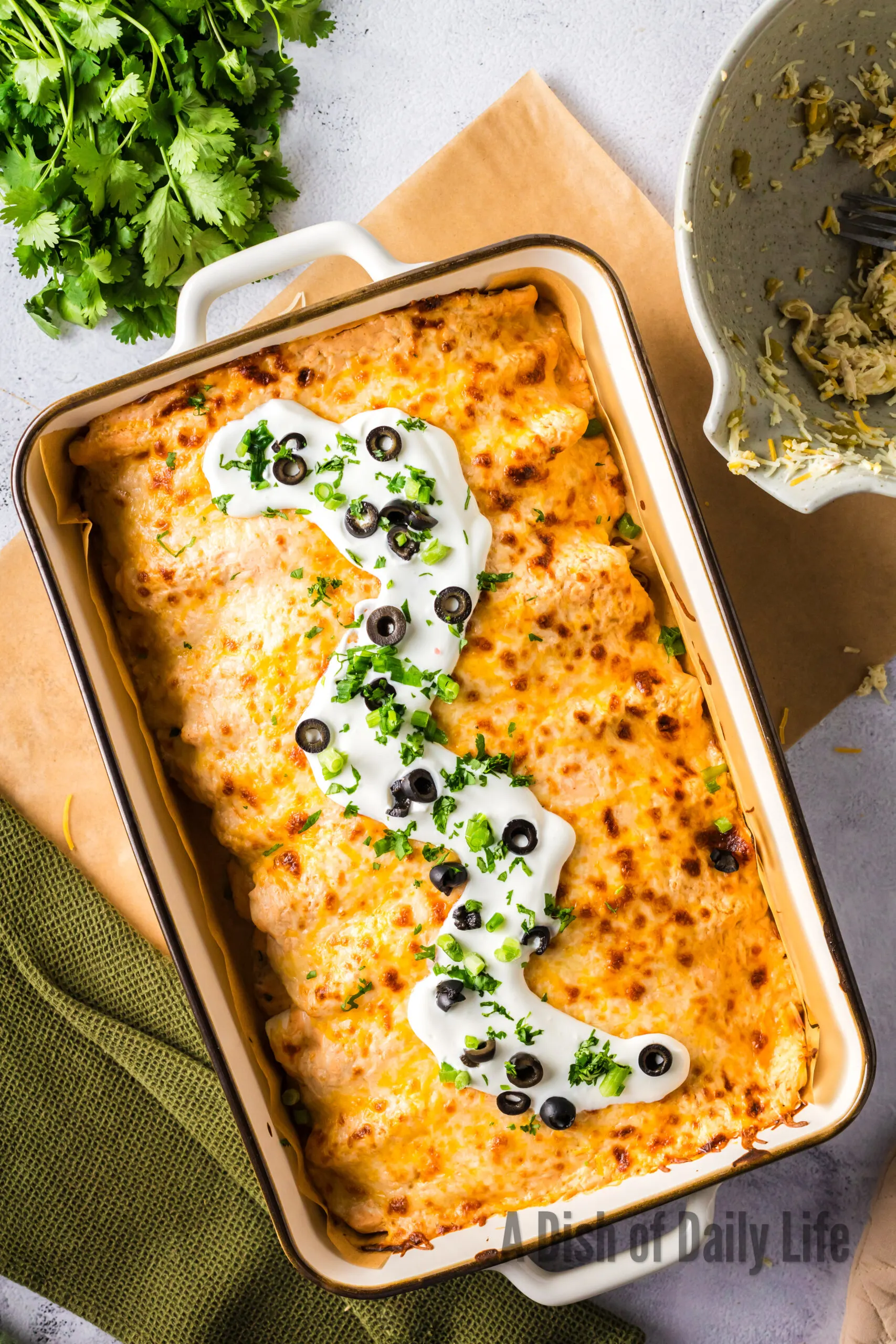 Sour Cream, green onions and black olives sprinkled on top of enchiladas in pan