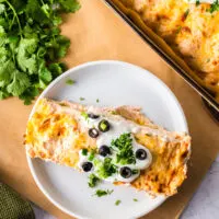 two enchiladas on a plate topped with sour cream, green onions and olives