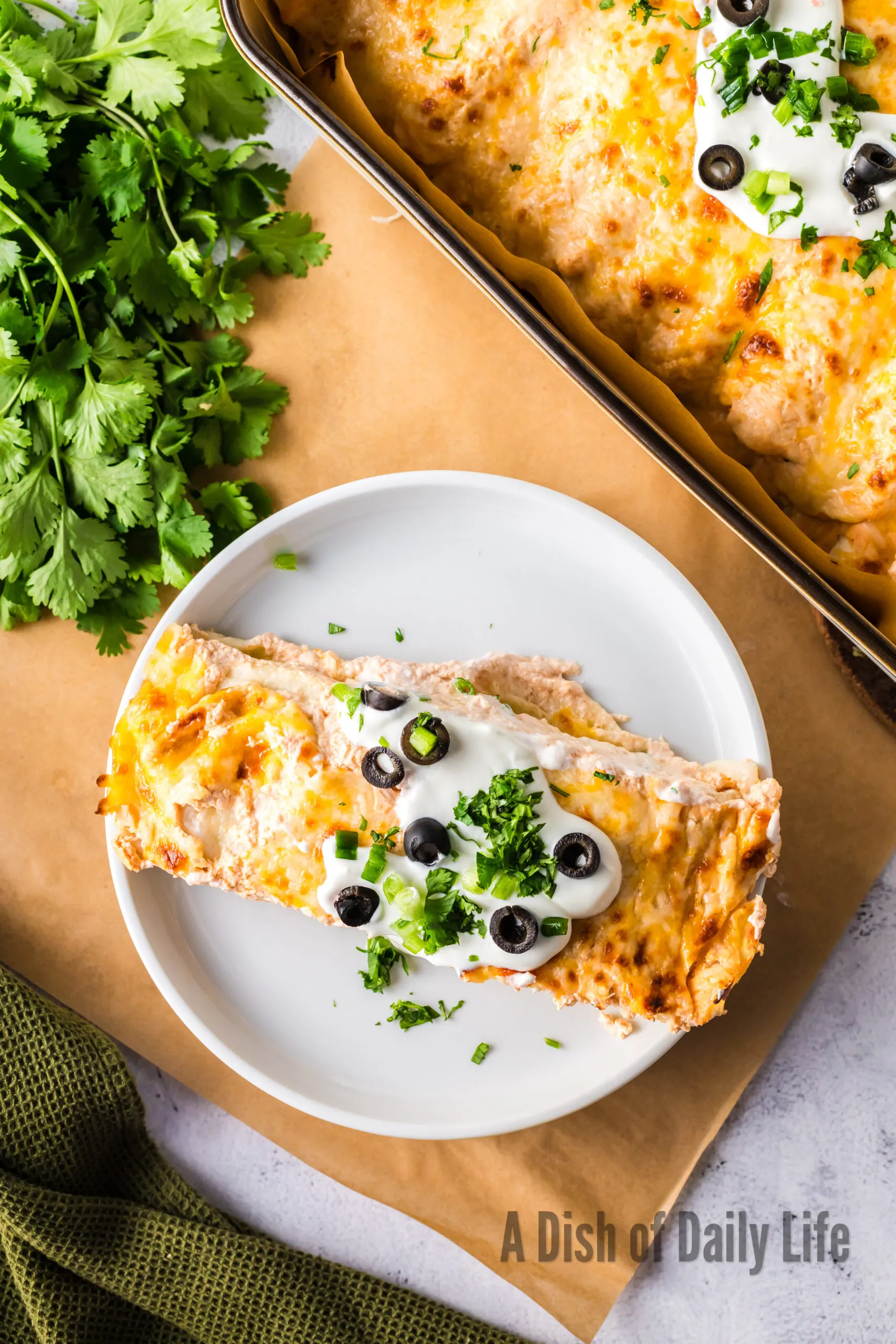 two enchiladas on a plate topped with sour cream, green onions and olives