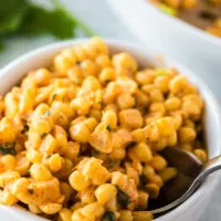 side view of corn in a single serving bowl with a spoon scooping some out.