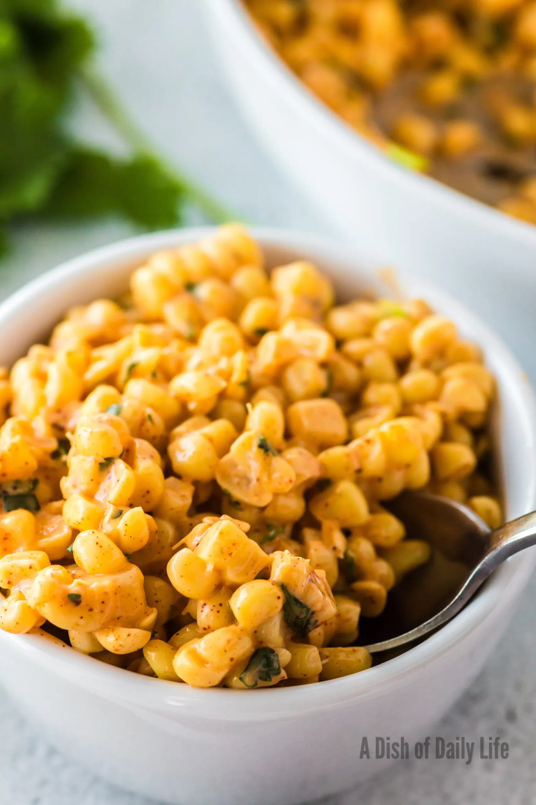 side view of corn in a single serving bowl with a spoon scooping some out.