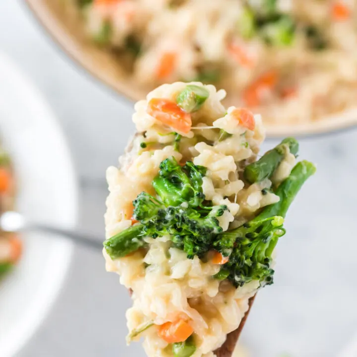 Wooden spoon scooping out risotto and holding it close to the camera lens.