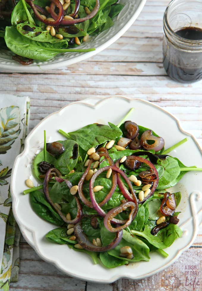 This Spinach Salad topped with sautéed red onions and pine nuts, and dressed with a Pomegranate Balsamic Vinaigrette is the perfect combination of tart and sweet. If you're looking for a simple salad with big flavors for your Thanksgiving or Christmas dinner menu, try this!