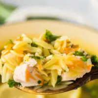 wooden spoon held above pot of soup full of orzo soup