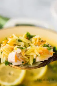 wooden spoon held above pot of soup full of orzo soup