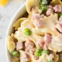 Zoomed in large portion of cooked pasta with ham and peas in a serving bowl.