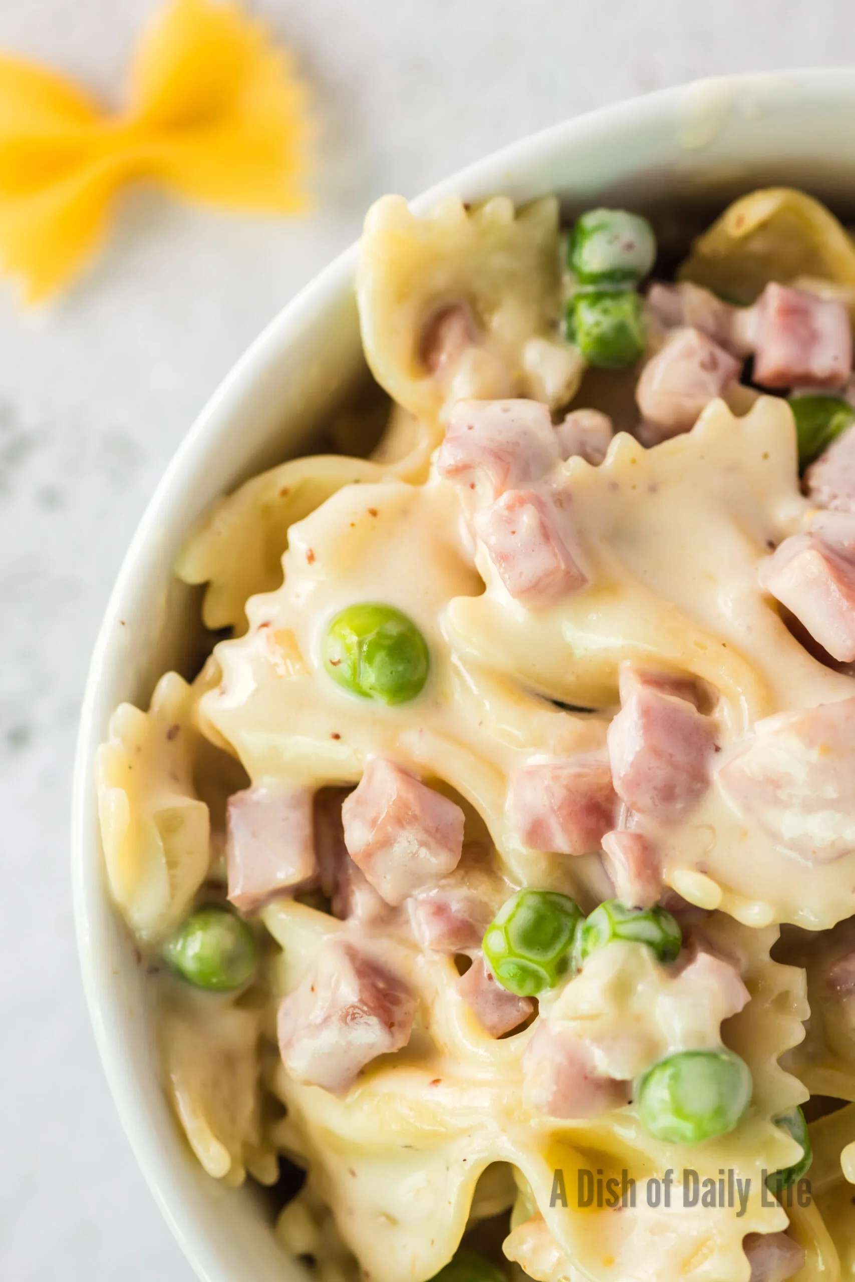 Zoomed in large portion of cooked pasta with ham and peas in a serving bowl.