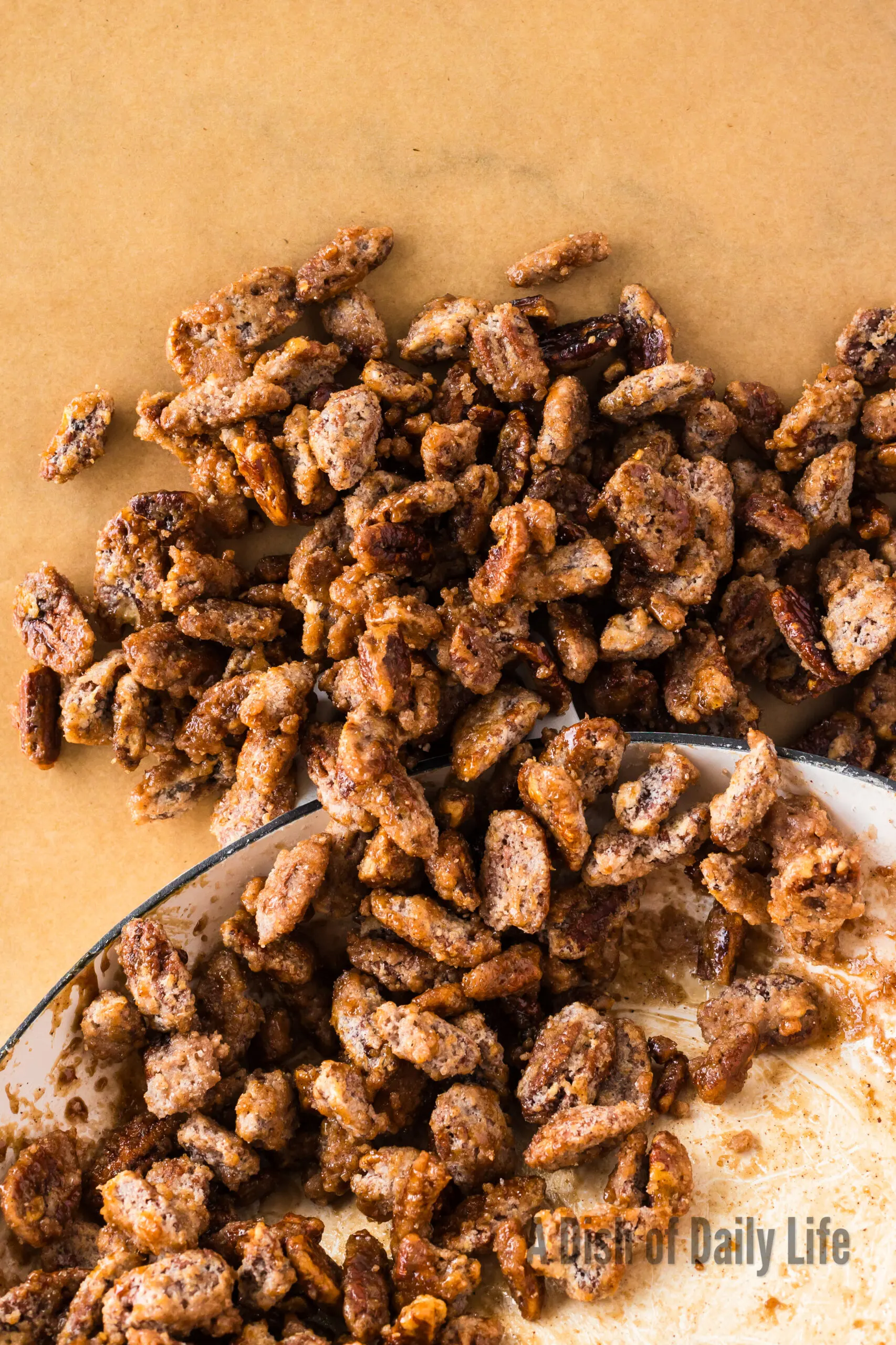 candied pecans being poured out of the skillet onto parchment paper