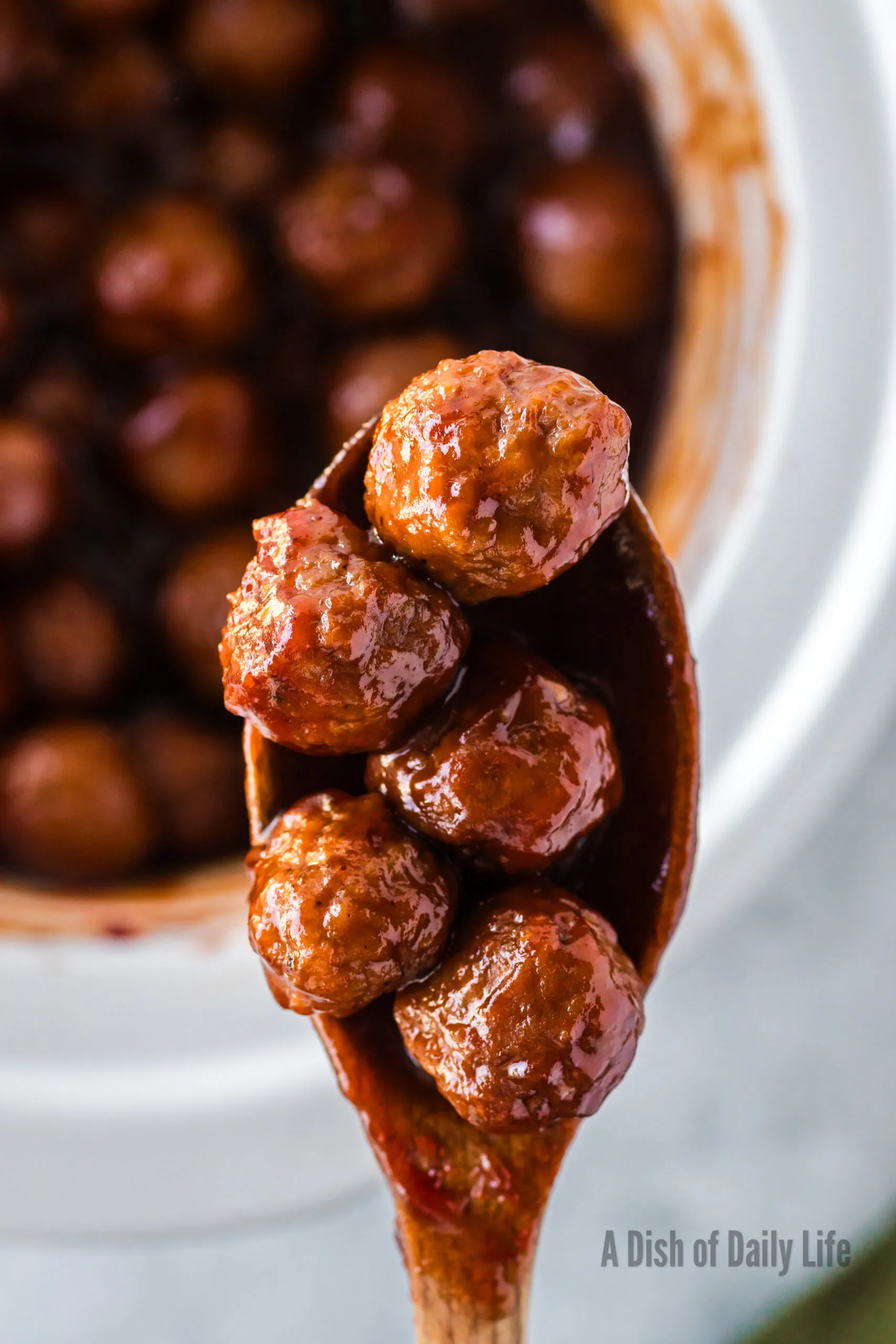 wooden spoon scooping meatballs out of crock pot.