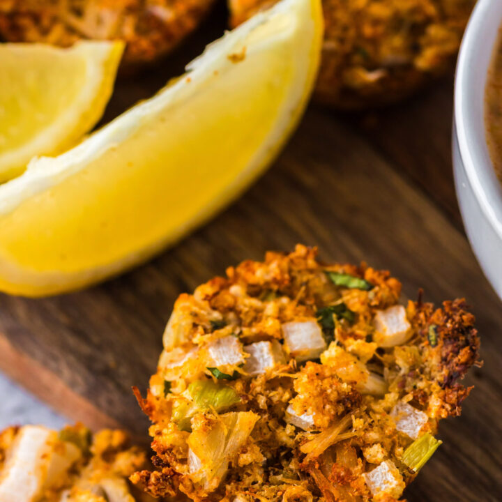 Zoomed in image of crab cake with lemon wedges on serving board.