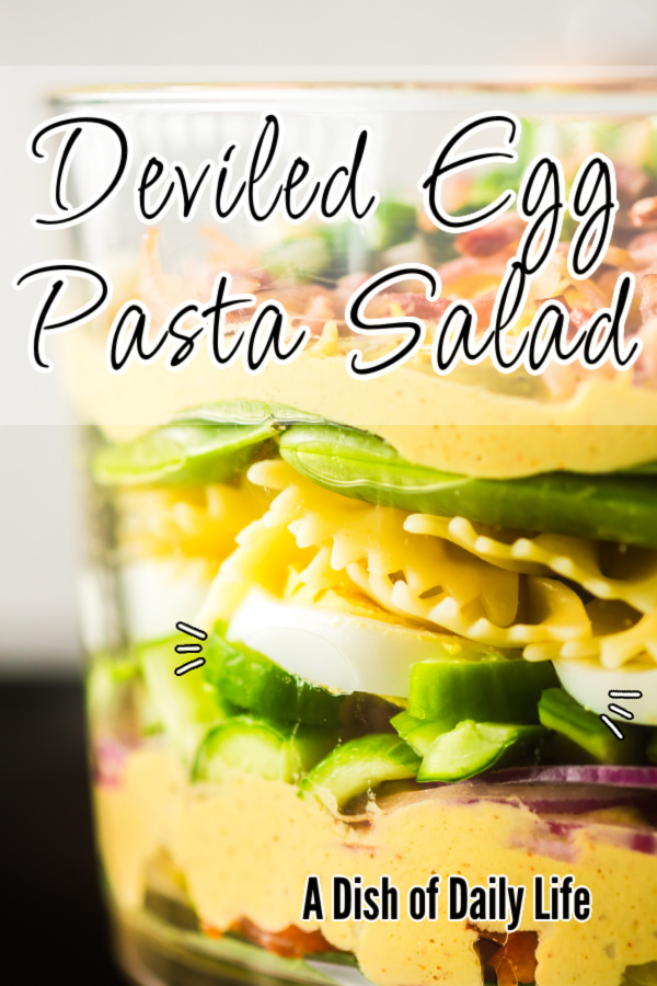 Main image for deviled egg pasta salad. Pasta salad is in a clear serving bowl to show layers.