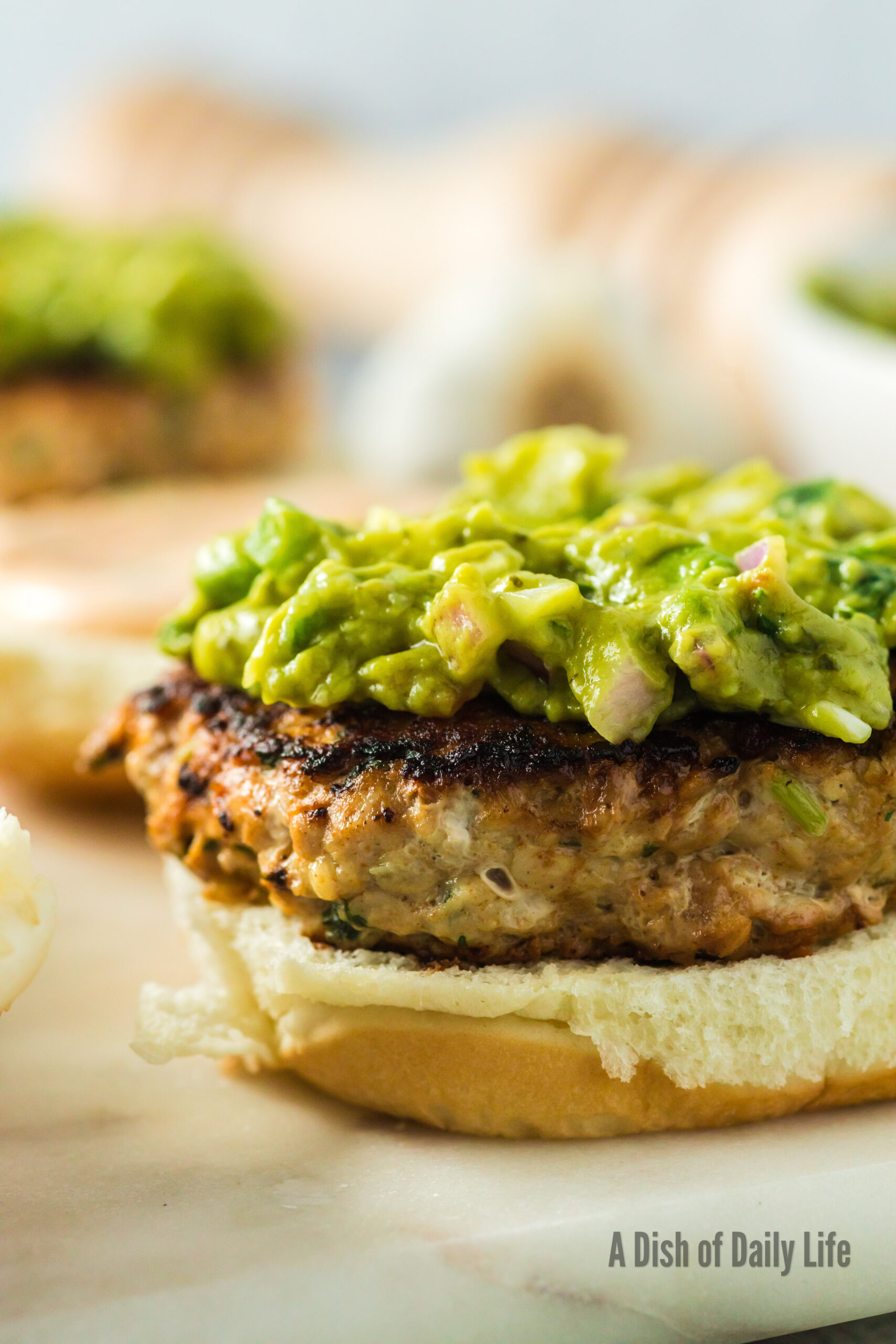 side view of chicken burger with avocado on top, top bun missing