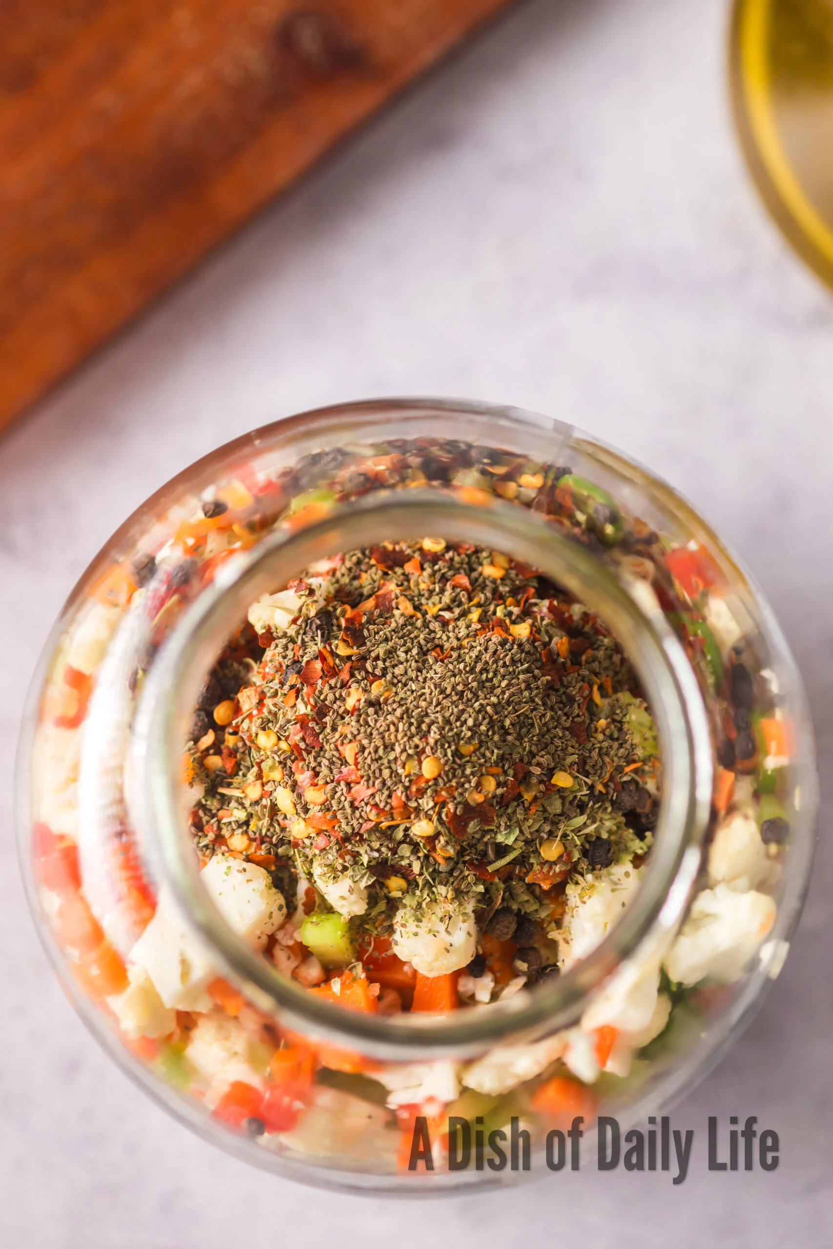 Vegetables transferred to a larger glass jar with spices added.