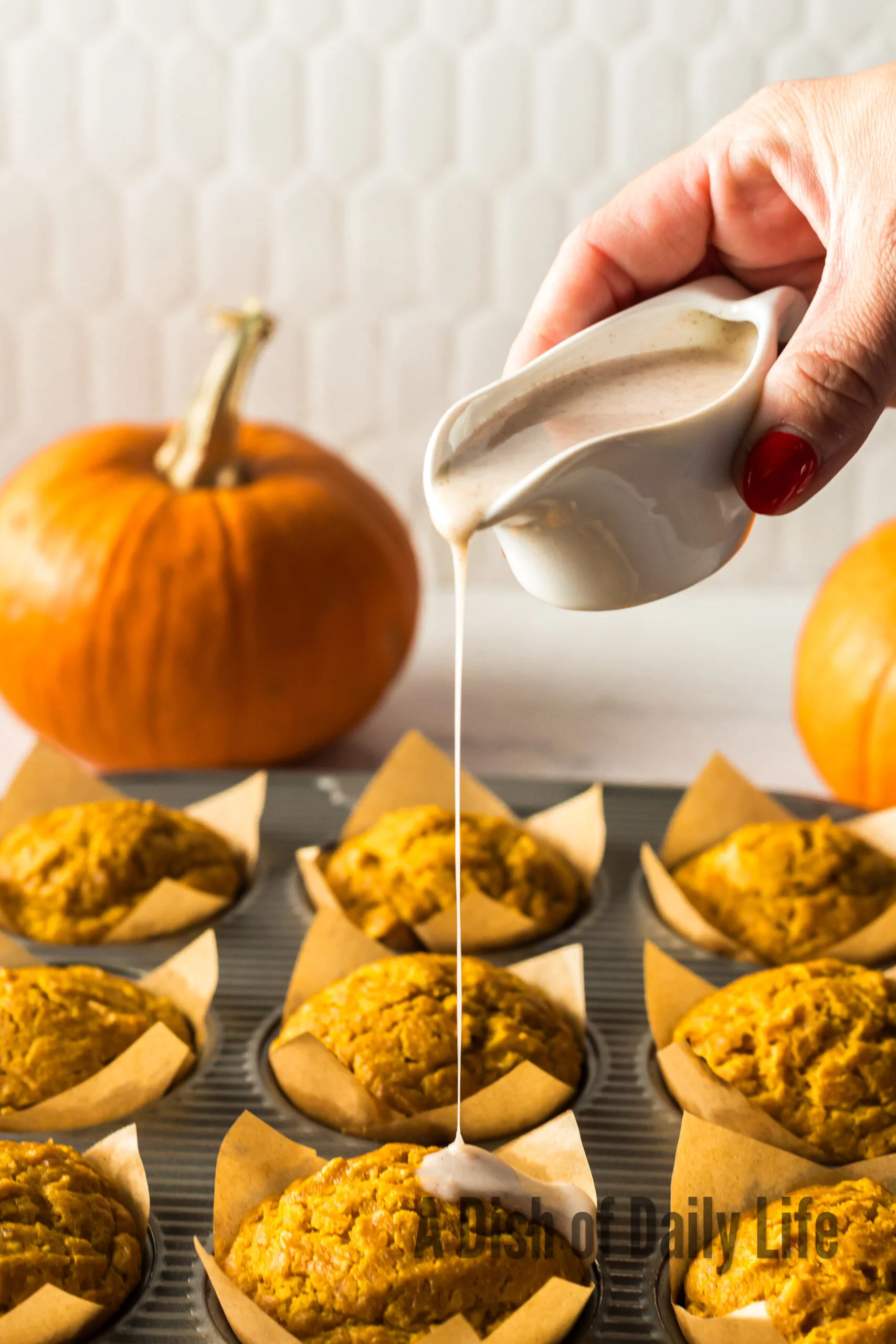 hand holding glaze over muffins and pouring it over the top of muffins.