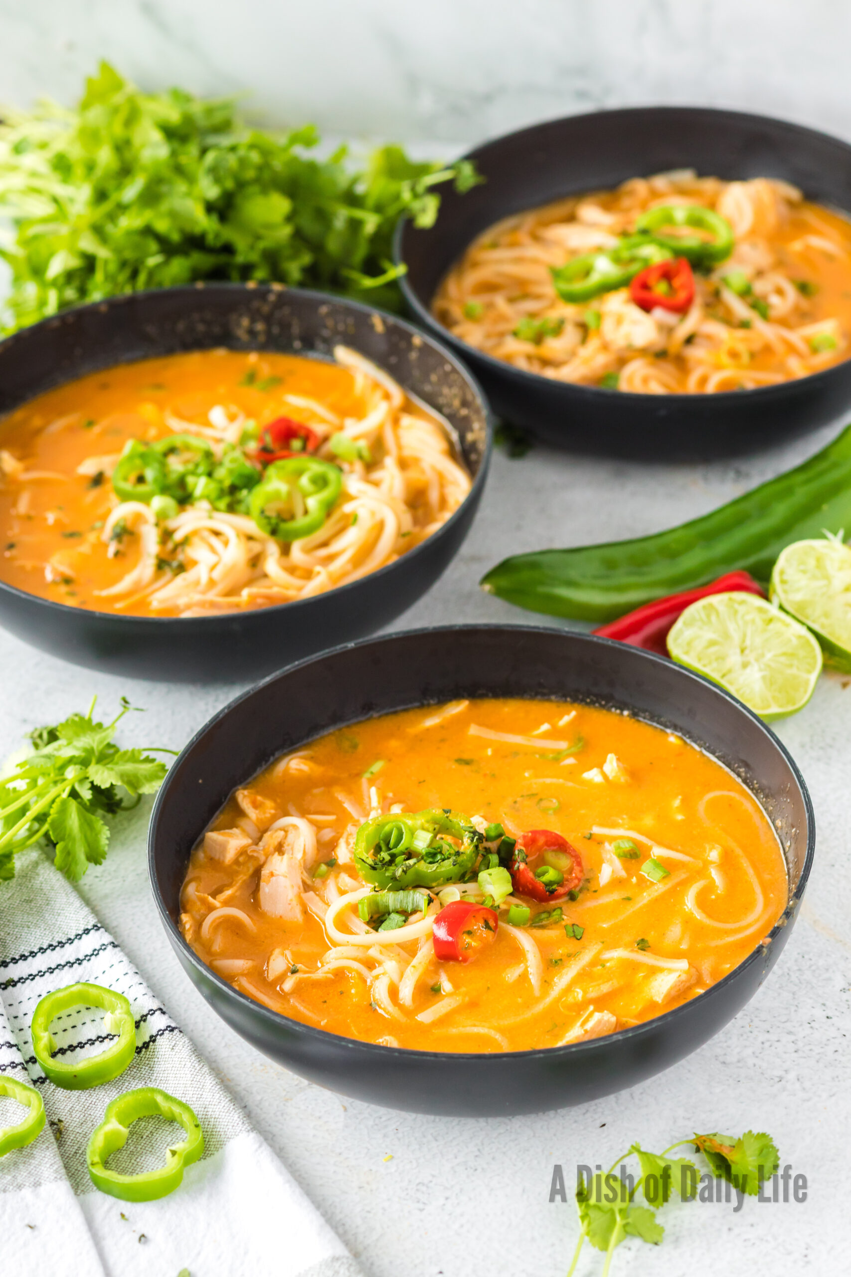 3 bowls of thai chicken noodle soup laid out, ready to serve