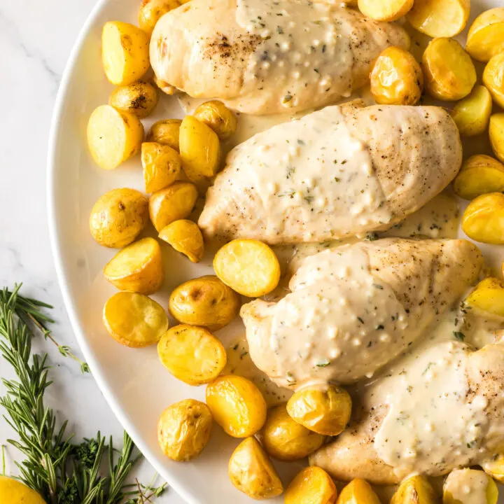 chicken and potatoes laid out on a serving tray with cream sauce poured over the top of chicken