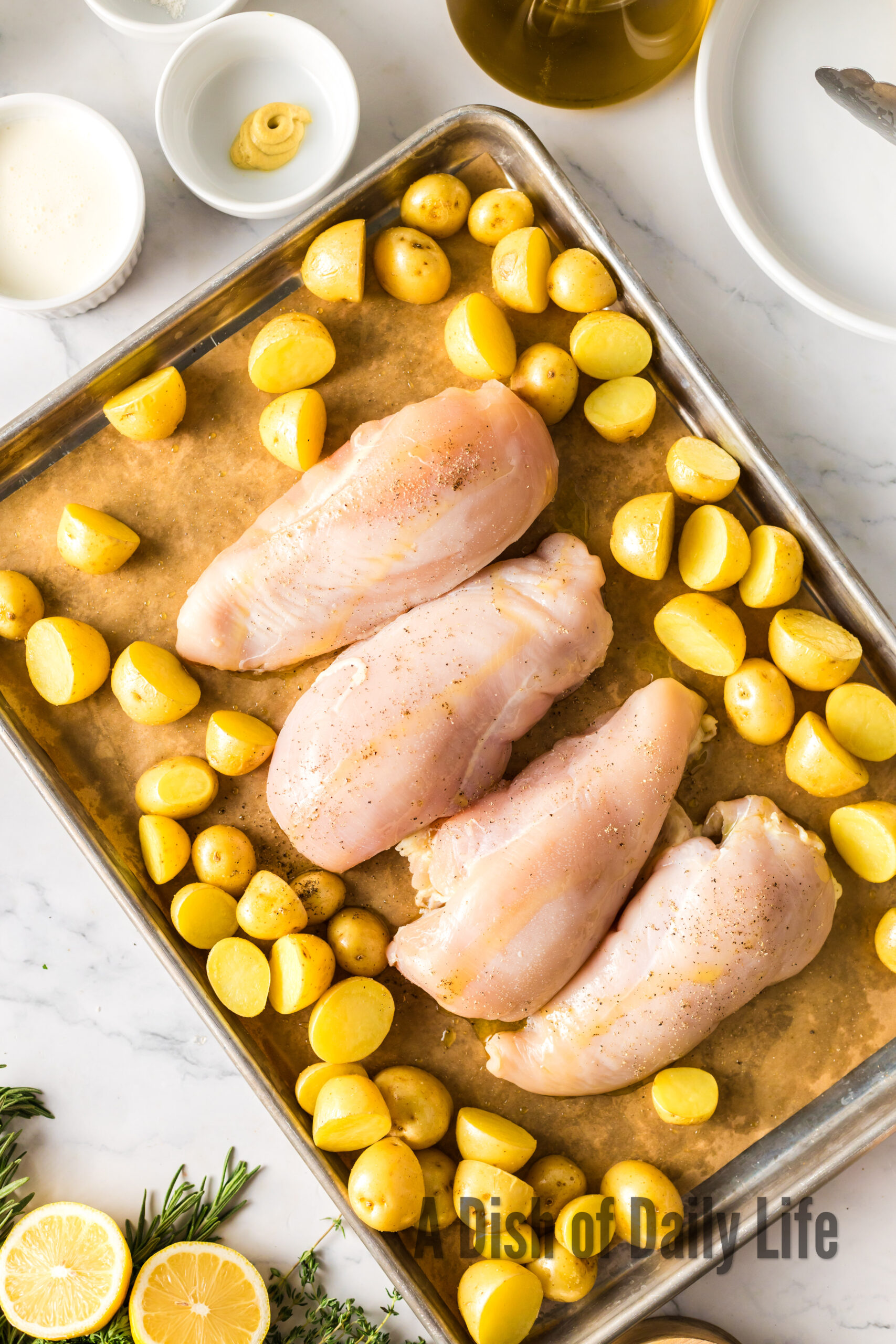 raw potatoes laid out on baking sheet with raw chicken breasts in the center.