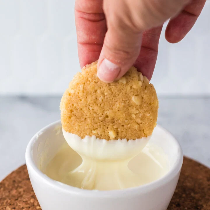 Hand dipping a single cookie into white chocolate.