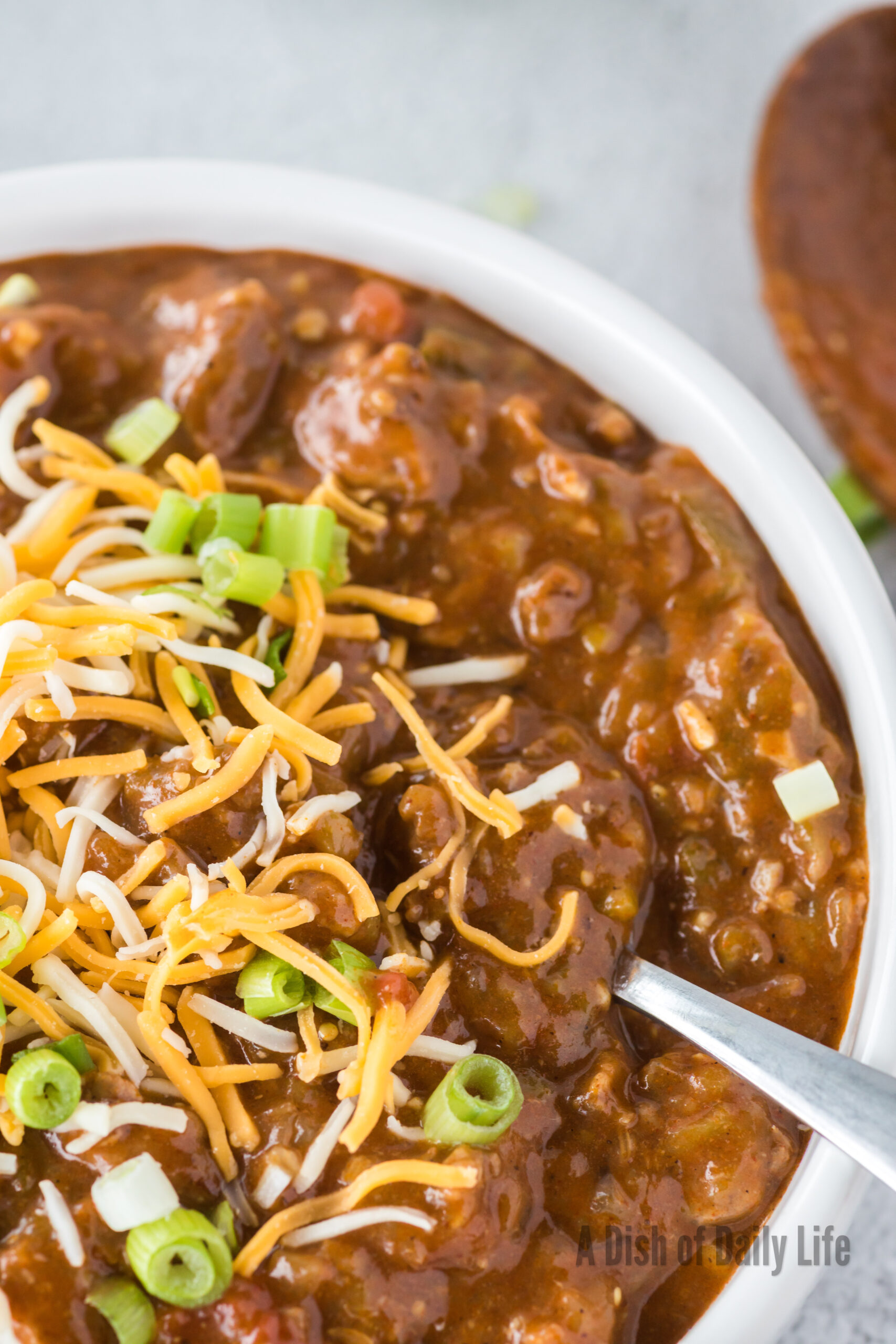 zoomed in image of a bowl of green pork chili with extra cheese and green onions on top