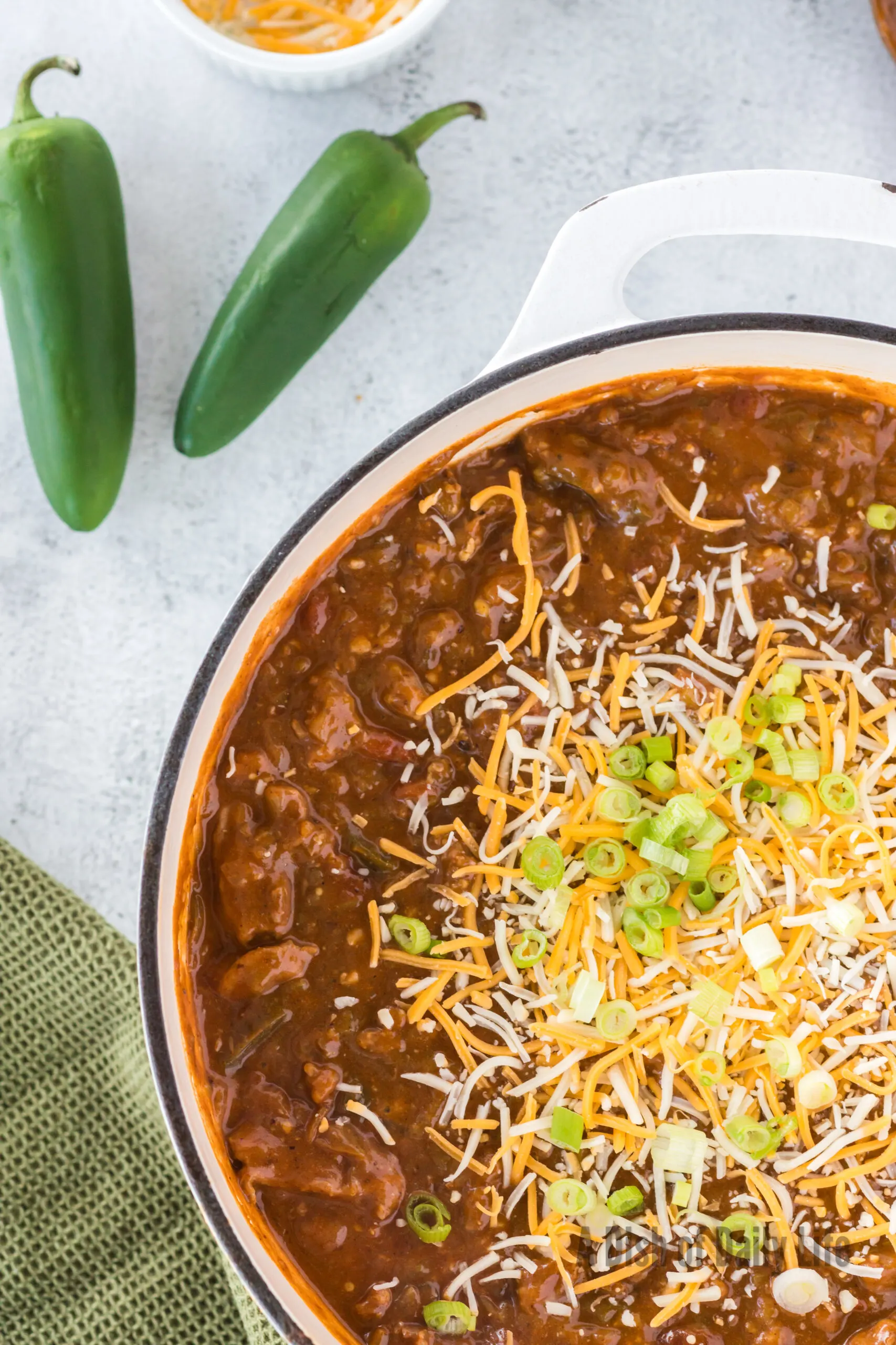 chili in pot topped with a pile of cheese and green onions