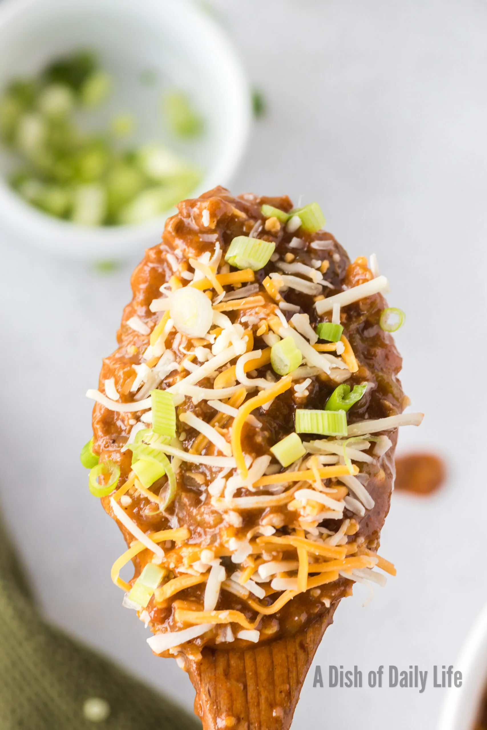 Wooden spoon scooping a portion of chili out of pot. Cheese and green onions sprinkled on top