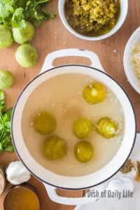 cooked tomatillos in pow with skins ready to remove
