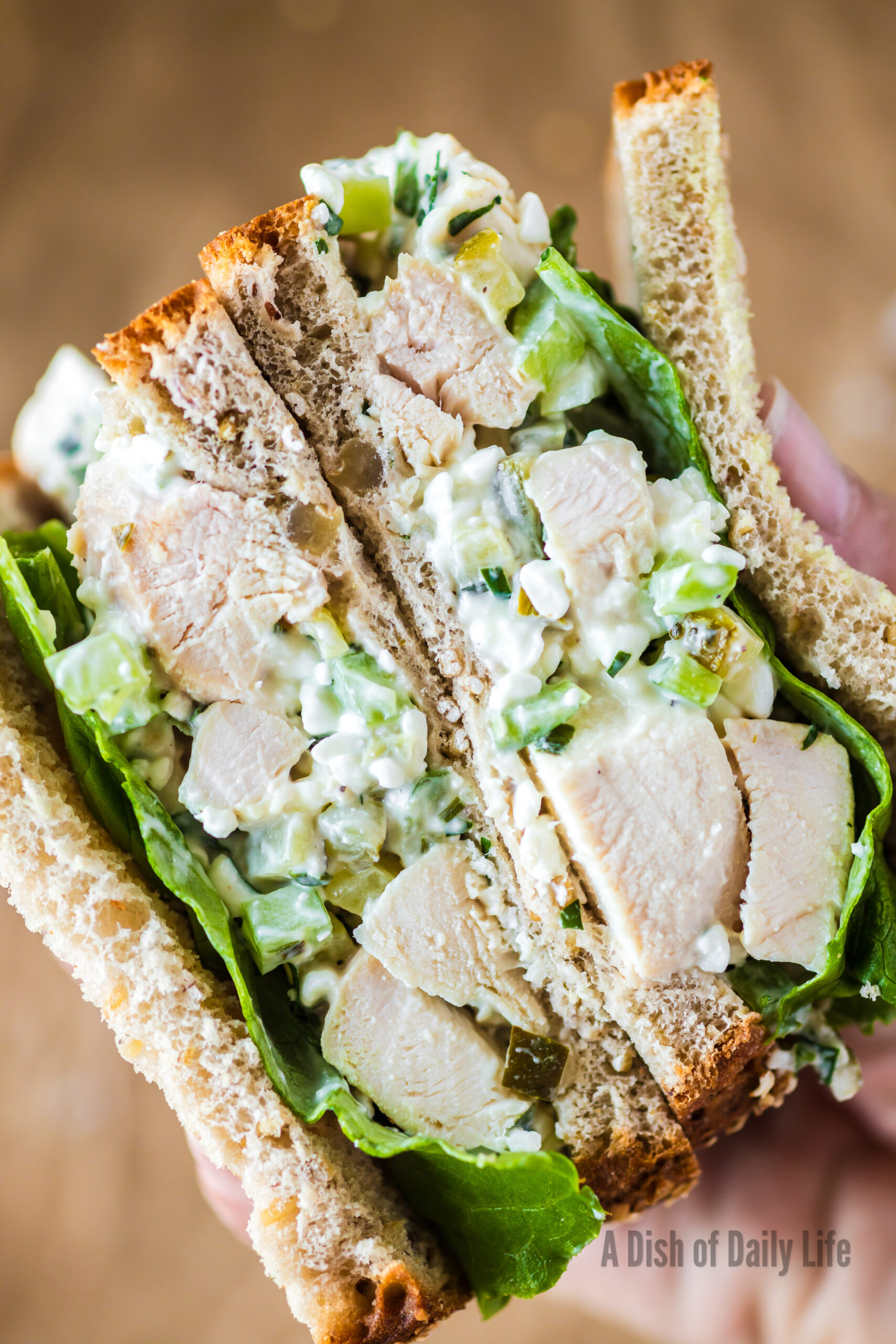 Hand holding a chicken salad sandwich cut in half to show yummy filling