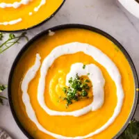 3 bowls of soup laid out on counter topped with additional creme fraiche and cilantro.