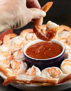 Shrimp being dipped in homemade cocktail sauce