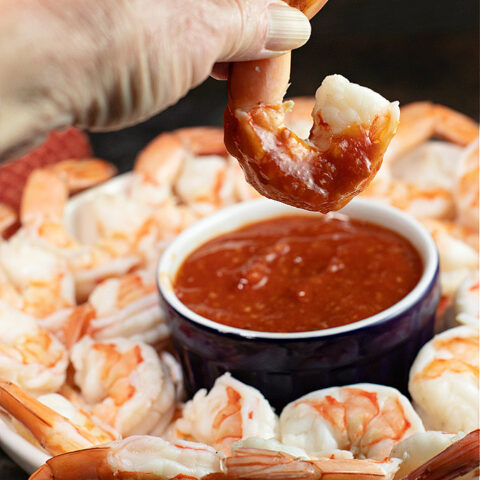 Shrimp being dipped in homemade cocktail sauce