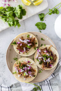 zoomed out image of 3 corn tortillas with shredded pork, red onions and cilantro on top
