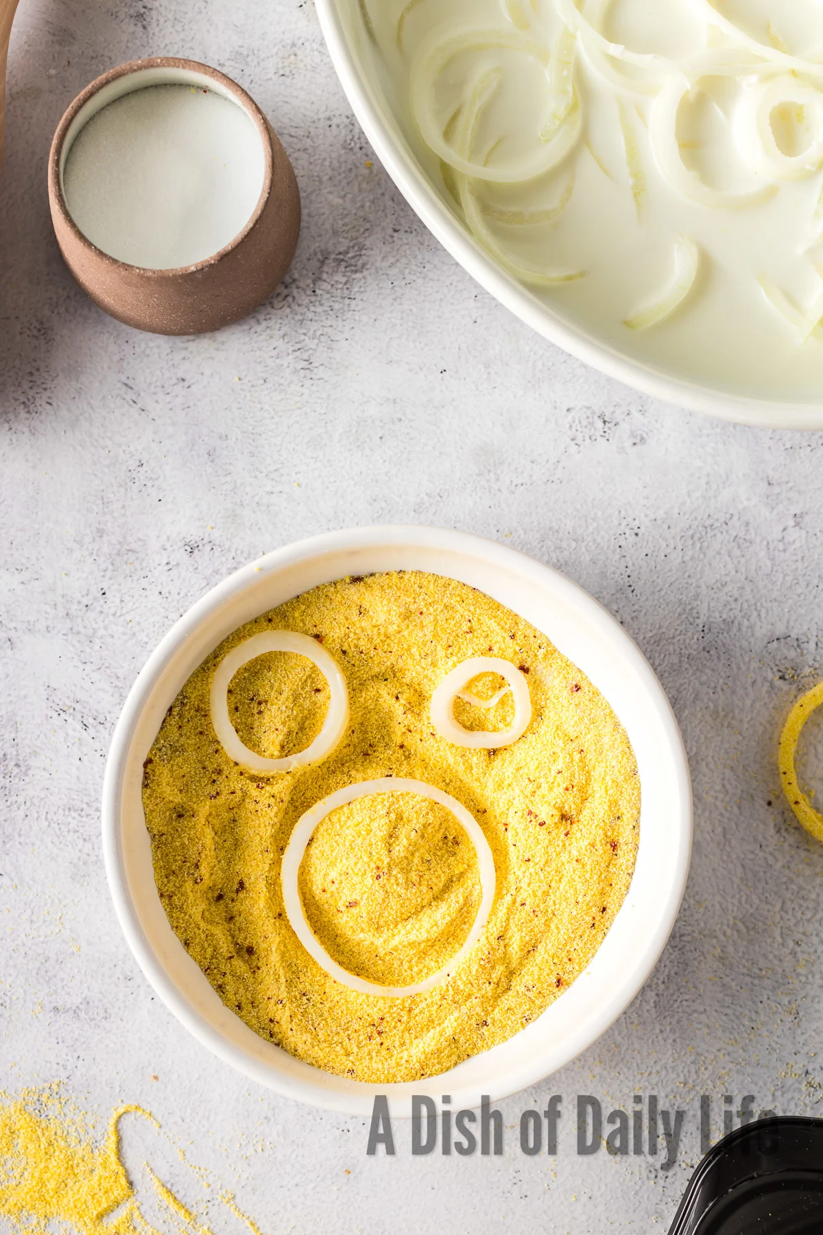 cornmeal, salt, black pepper and aleppo pepper in a bowl mixed up with buttermilk onions being coated