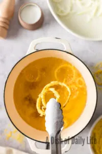 tongs pulling out 2 crispy fried onions from hot oil