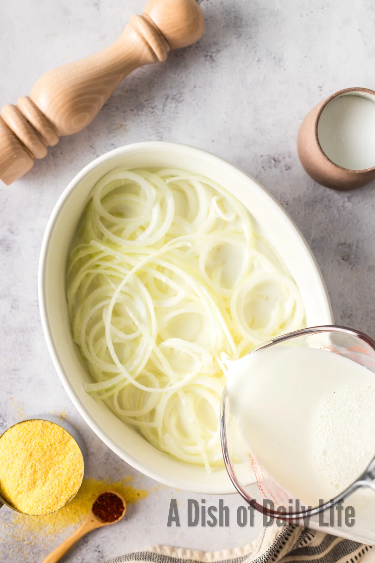 thinly sliced onions in a bowl with buttermilk being poured over the top.