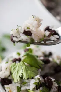 fork full of rice and black beans and being lifted above bowl